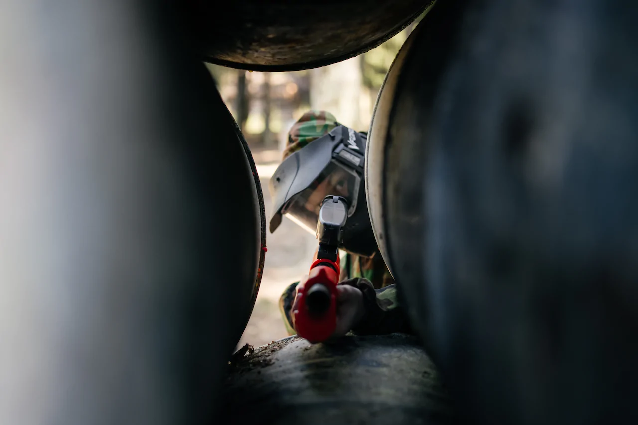 Участник детского пейнтбола в маске и форме целится из маркера