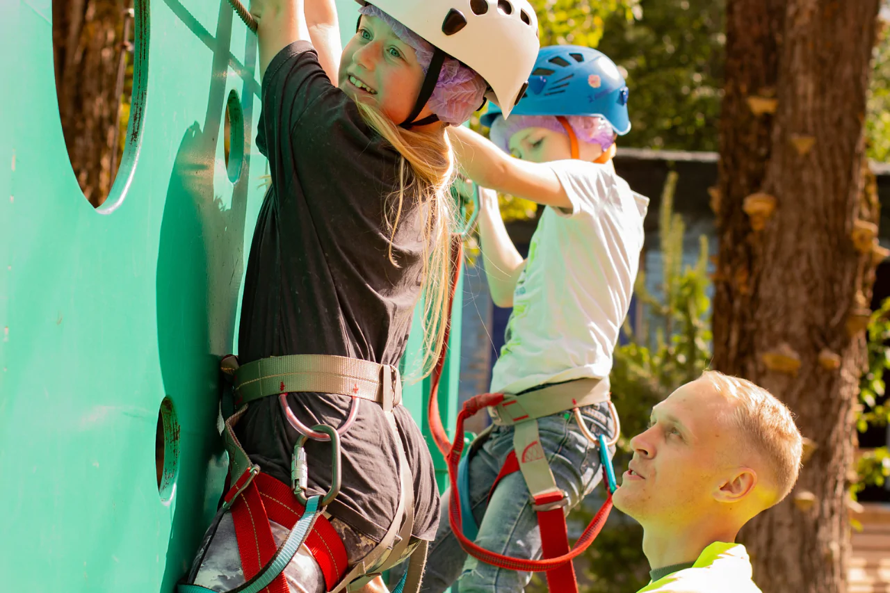 Инструктор помогает ребёнку пройти верёвочную трассу